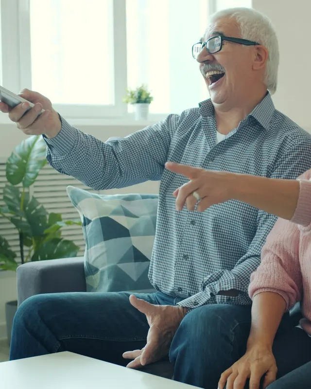 An older couple pointing at the TV and laughing