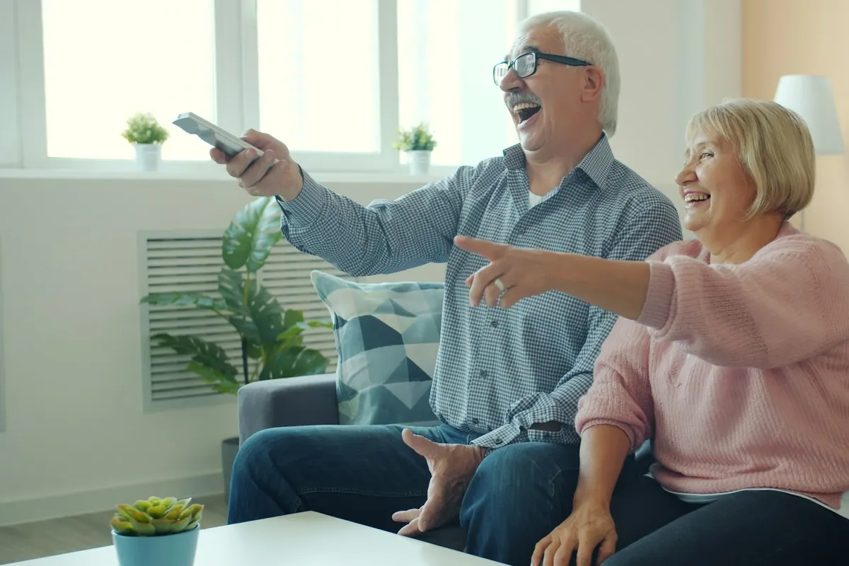 An older couple laughing and pointing at the TV